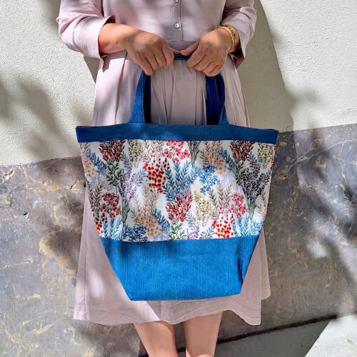 Schnittmuster „Carry & Go" – selbstgenähte Tasche mit Boden in Blau, getragen von einer Frau, mit floralem Blumenmuster und blauem Bodenteil, Tragegriffen bzw. Eingriffumrandung