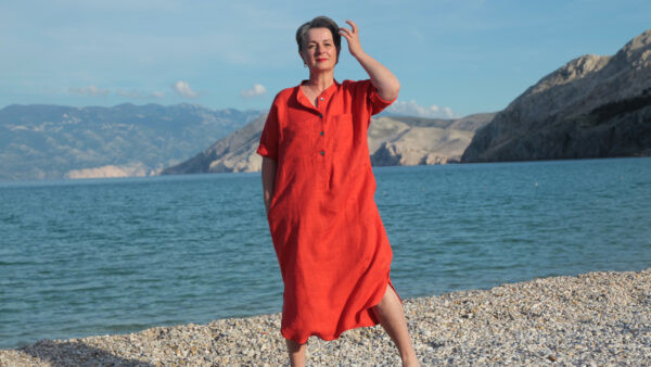 Frau mit dunklen kurzen Haaren trägt rotes legeres Leinenkleid am Strand. Das Kleid ist ein patternhack der Bluse Lilia_B von B-patterns