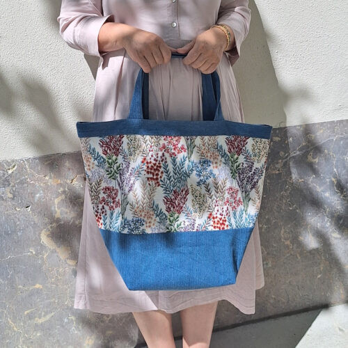 Schnittmuster „Carry & Go" – selbstgenähte Tasche mit Boden in Blau, getragen von einer Frau, mit floralem Blumenmuster und blauem Bodenteil, Tragegriffen bzw. Eingriffumrandung