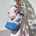 Schnittmuster „Carry & Go" – selbstgenähte Tasche mit Boden in Blau, getragen von einer Frau, mit floralem Blumenmuster und blauem Bodenteil, Tragegriffen bzw. Eingriffumrandung- Seitliche Ansicht