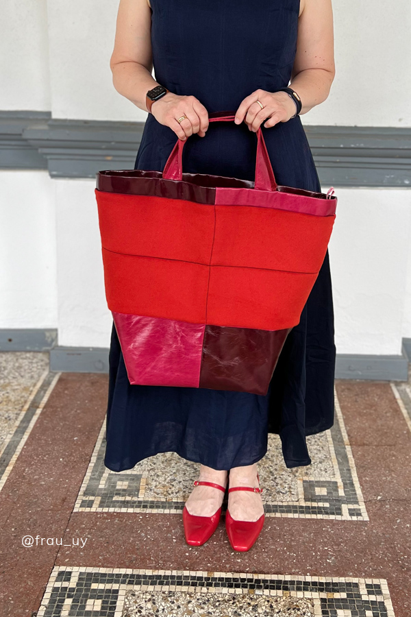 Frau in dunkelblauem Kleid und roten Schuhen hält eine selbstgenähte große Tasche aus rotem Stoff mit Lederdetails in Rot- und Bordeauxtönen genäht nach dem Schnittmuster "Carry&Go" bpatterns
